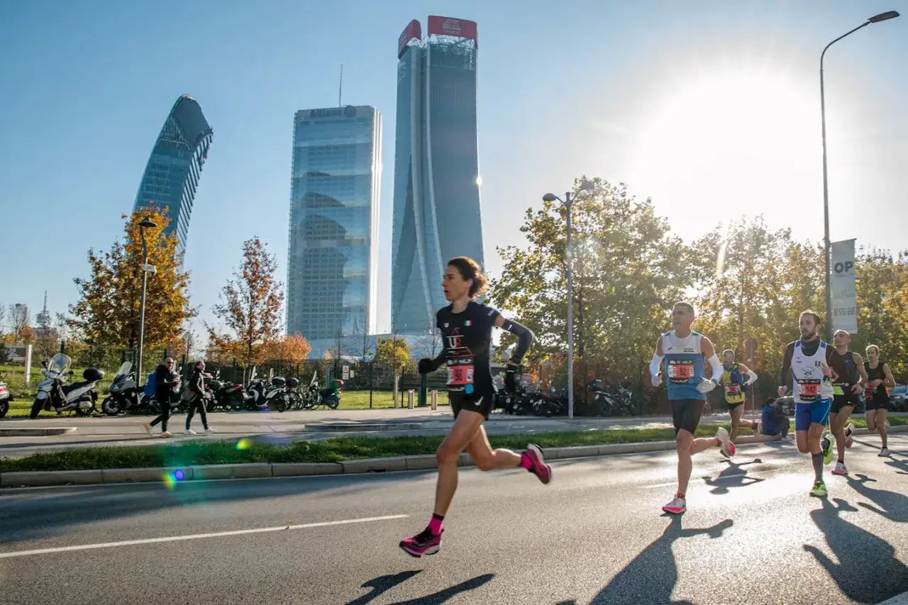 Corredores compiten en la **media marat&oacute;n Mil&aacute;n** con modernos rascacielos de fondo.