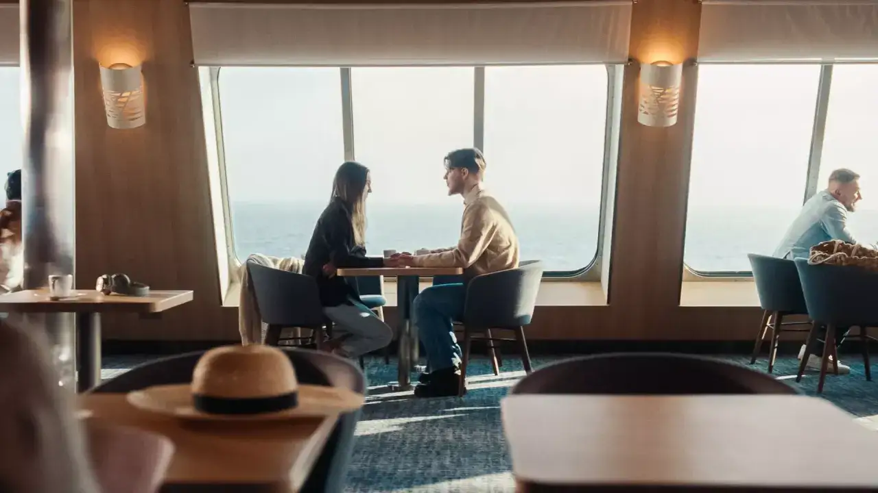 Para zakochanych trzyma się za ręce przy stoliku na promie Stena Spirit, w tle morze i niebo.