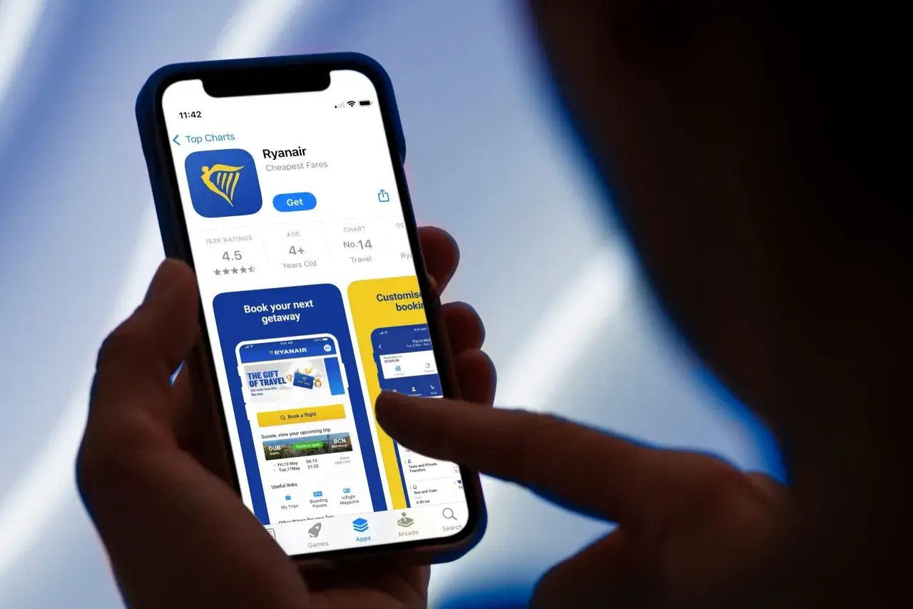 Osoba przegląda aplikację Ryanair, szukając tanich lotów. Widoczna jest karta pokładowa Ryanair z informacjami o podróży.