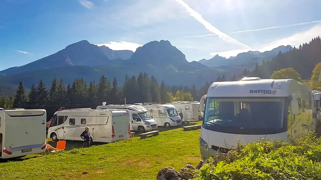 Słoneczny dzień na kempingach w Czarnogórze. Kampery zaparkowane na zielonej trawie, w tle majestatyczne góry.