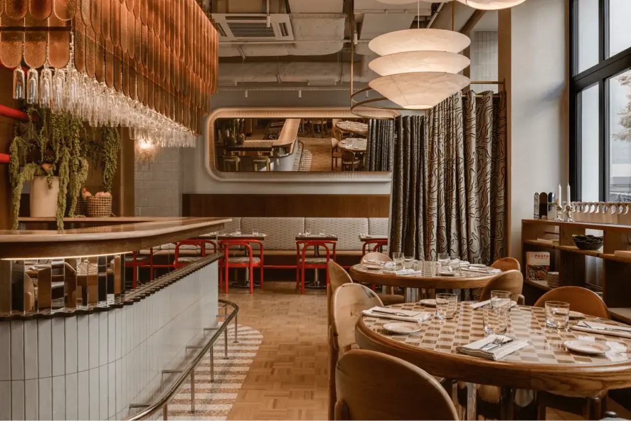 Przytulne bistro z drewnianymi stołami i czerwonymi krzesłami. Lustro odbija wnętrze, tworząc wrażenie większej przestrzeni.