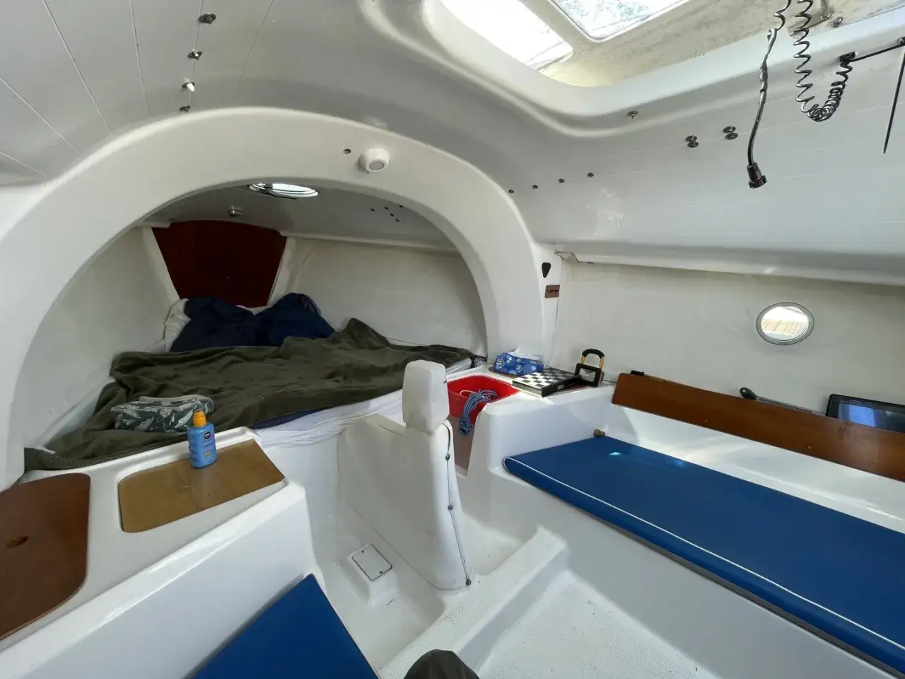 Intérieur du first 210, lit préparé avec couverture verte, coussins bleus, et une bouteille de crème solaire.