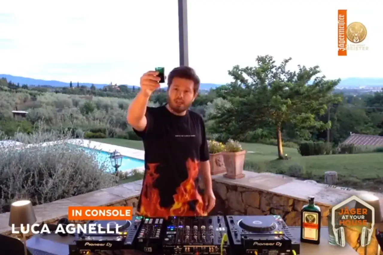 Luca Agnelli, un artista di musica elettronica, brinda con un bicchierino davanti a un paesaggio collinare.