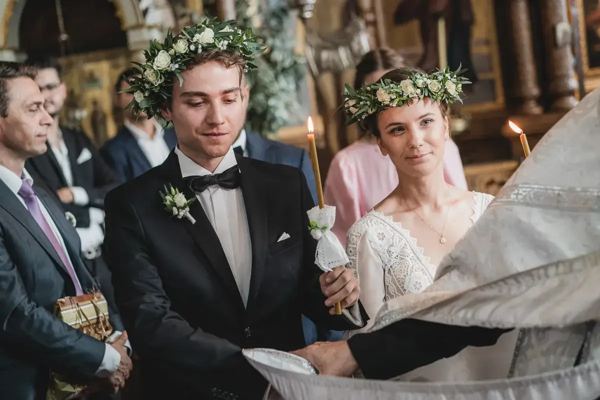 Młoda para w wiankach z kwiat&oacute;w podczas ślubu prawosławnego. Trzymają zapalone świece, symbolizujące światło Chrystusa.