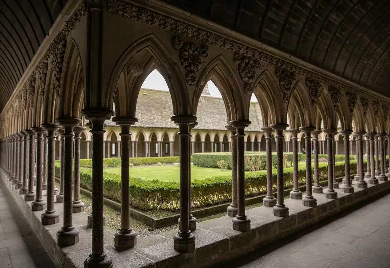 Gotische Arkaden im Mont Saint Michel innen. Ein gr&uuml;ner Garten mit B&uuml;schen und Rasen erstreckt sich hinter den S&auml;ulen.