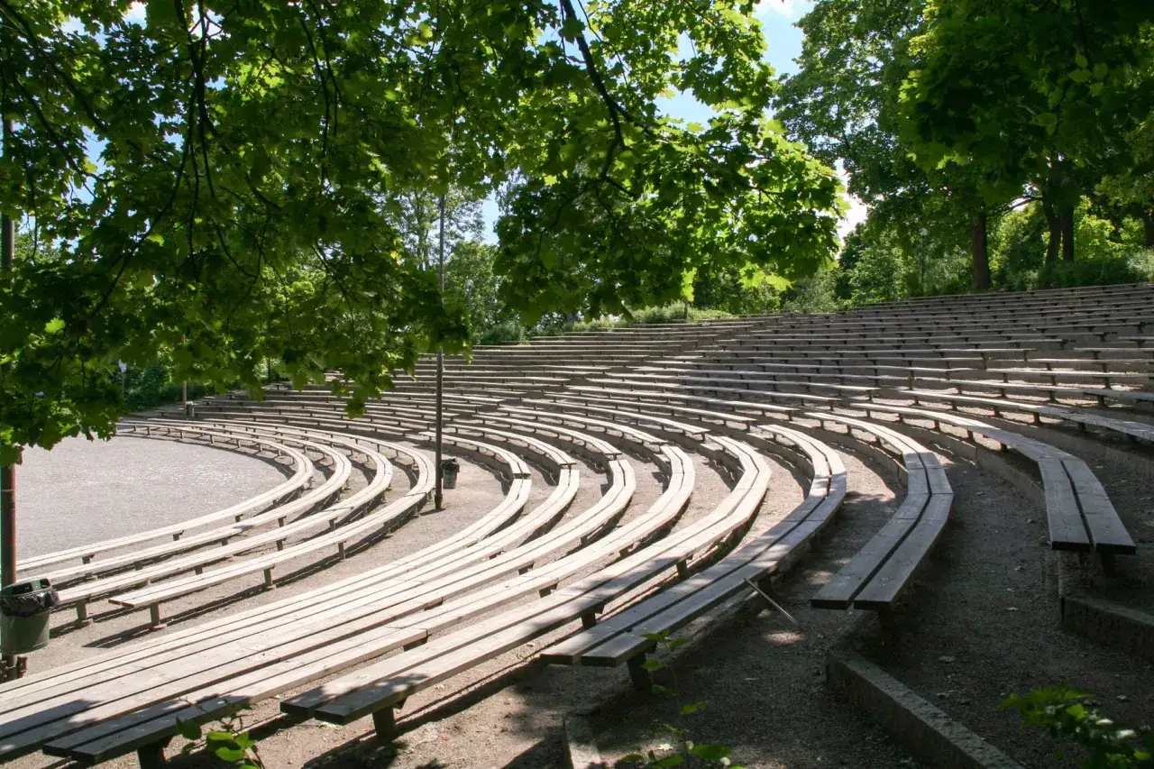 Tomma tr&auml;b&auml;nkar i en cirkul&auml;r amfiteater i Vitabergsparken teater, omgivna av gr&ouml;na tr&auml;d.