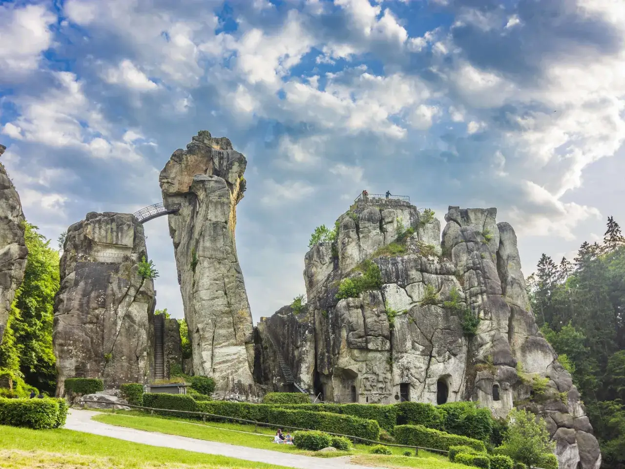 Die Externsteine, eine der faszinierendsten Attraktionen NRWs, ragen majest&auml;tisch in den Himmel. Eine Br&uuml;cke verbindet zwei Felsformationen, w&auml;hrend Besucher die Aussicht genie&szlig;en.