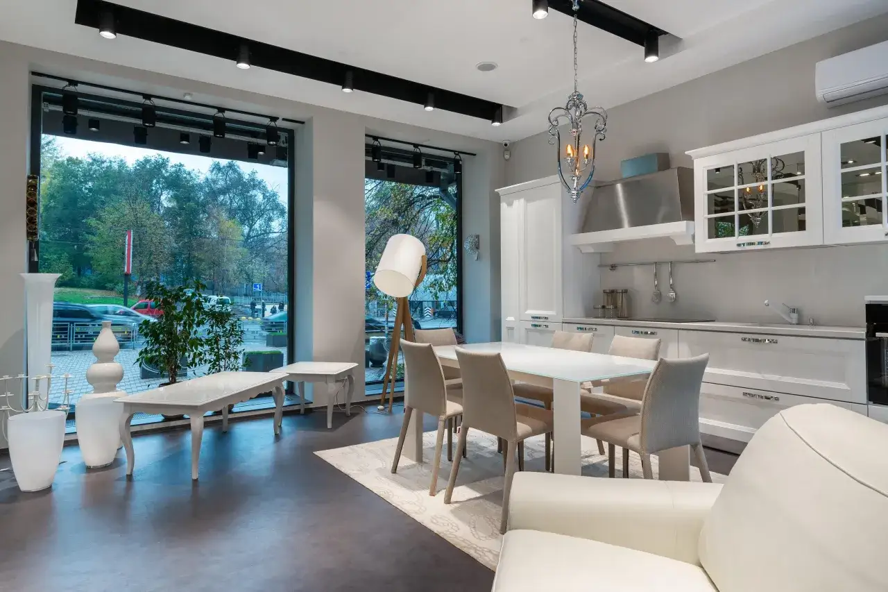 Espacio moderno de cocina sal&oacute;n comedor de 30 m2 con mesa blanca, sillas beige, sof&aacute; blanco y grandes ventanales.