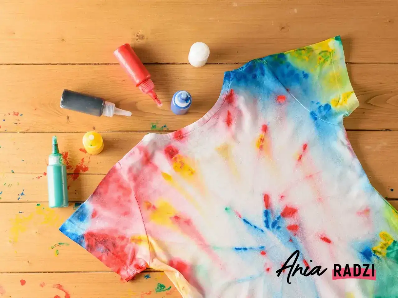 Kolorowa koszulka po farbowaniu ubrań techniką tie-dye, obok buteleczki z farbami.