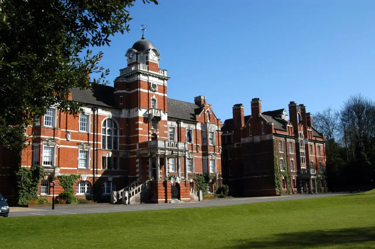 Bâtiments en briques rouges avec une tour d'horloge, typiques de l'université de Greenwich, sous un ciel bleu clair.