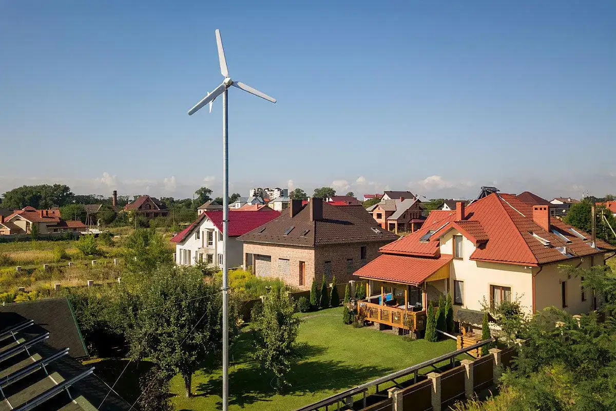 Wiatrak na podwórku, być może turbina wiatrowa bez pozwolenia, na tle domów z czerwonymi dachami.