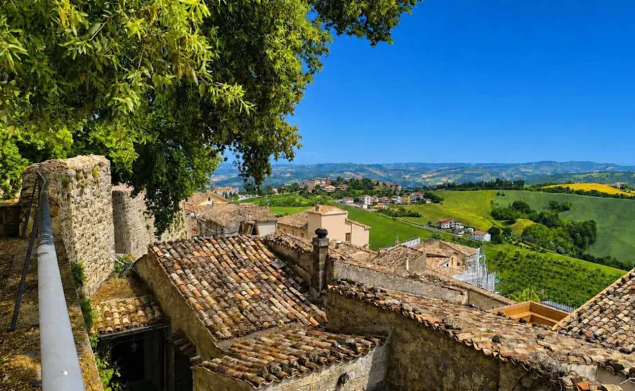Panoramica di borghi da visitare in provincia di Teramo, con tetti in cotto e colline verdi sotto un cielo azzurro.