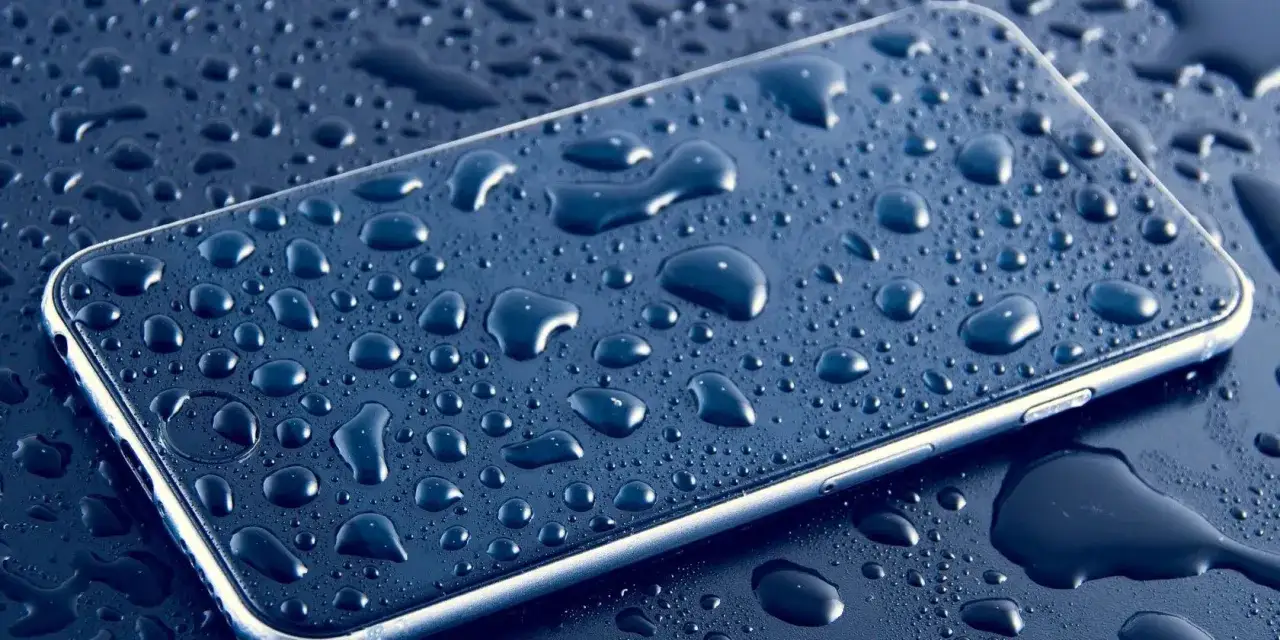 Smartfon pokryty kroplami wody. Dowiedz się, jak wysuszyć port USB po zalaniu, aby uniknąć uszkodzeń.