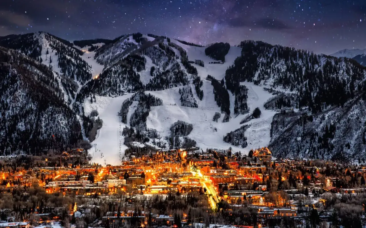 Winterabend in Aspen, Colorado. Lichter der Stadt leuchten unter schneebedeckten Bergen und Sternenhimmel.