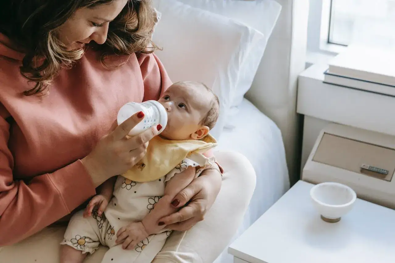Mamma nutre il suo neonato con il biberon. Sembra che il piccolo mangi troppo, con gli occhietti sgranati e la bocca piena.