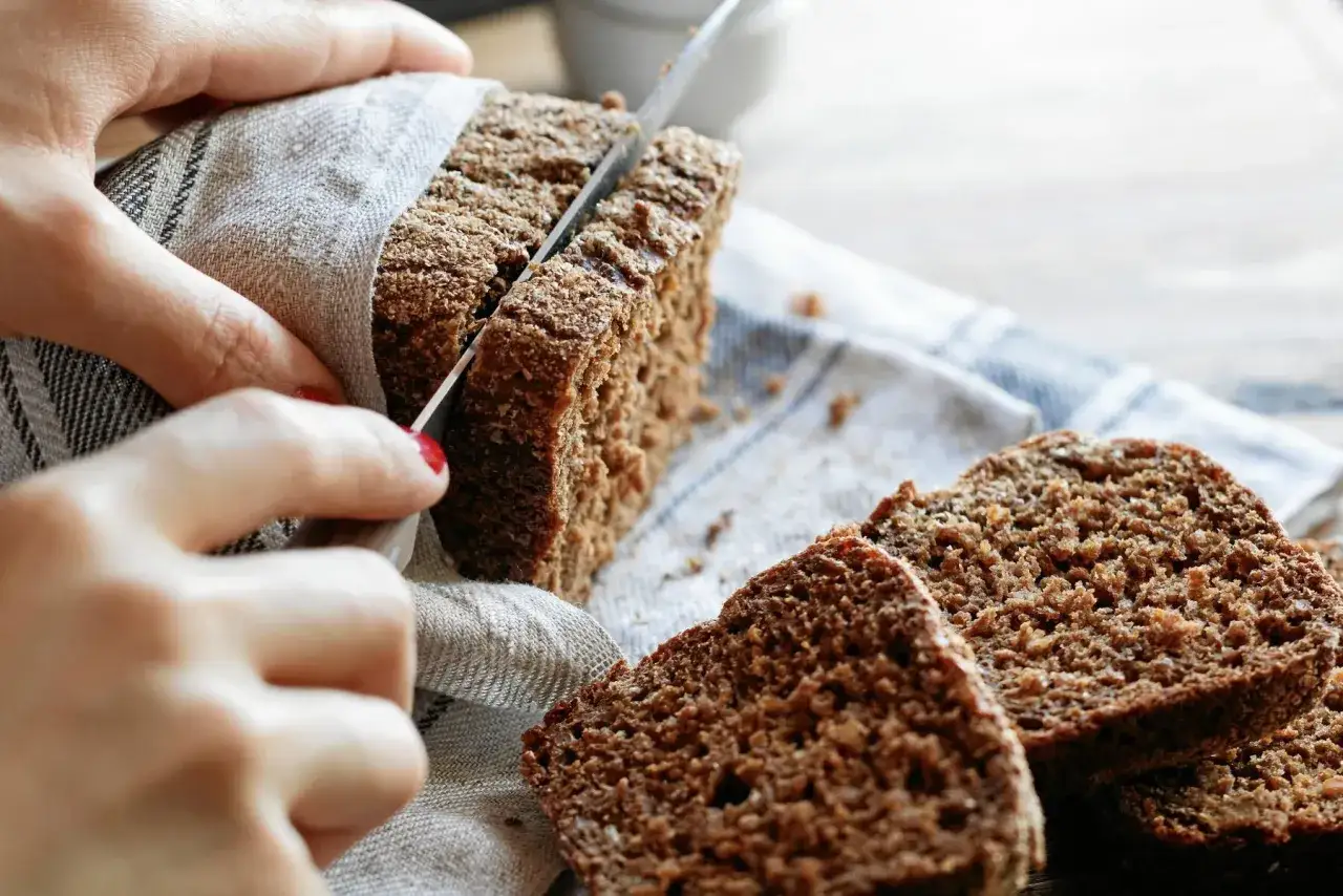 Här skärs en bit av ett mörkt, saftigt bröd. Ett perfekt kavring recept för hembakat.