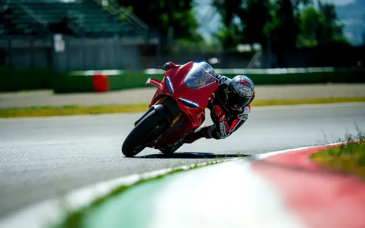 Motocyklista w kasku pochyla się na torze wyścigowym na czerwonym Ducati Panigale V4, z kolanem prawie dotykającym asfaltu.