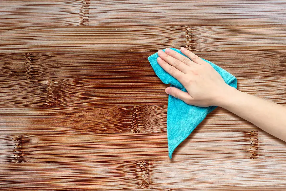 Main d'une personne utilisant un chiffon bleu pour nettoyer une surface en bois. Apprenez comment nettoyer des portes en bois pour un &eacute;clat parfait.