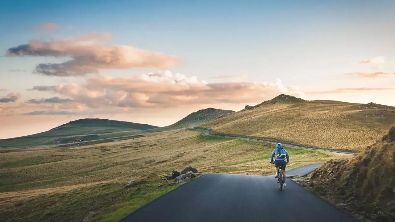 Ciclista en una carretera escénica, ideal para rutas en bici para principiantes. Paisaje montañoso al atardecer.