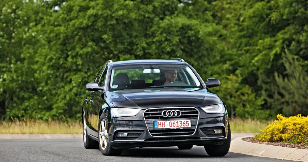 Czarny Audi A4 B8 na drodze, kierowca w okularach. Typowe usterki tego modelu mogą dotyczyć elektroniki i układu napędowego.