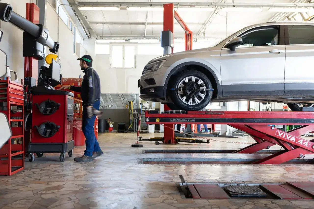 Un meccanico esegue la manutenzione pneumatici su un'auto sollevata in officina, utilizzando attrezzature specializzate per garantire la sicurezza e le prestazioni.