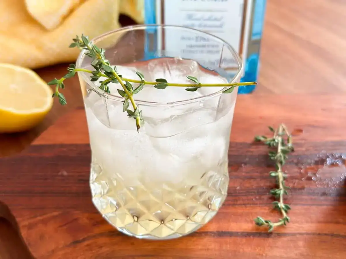 Orzeźwiający gin z tonikiem i cytryną, ozdobiony gałązką tymianku. Idealny na letnie popołudnie.