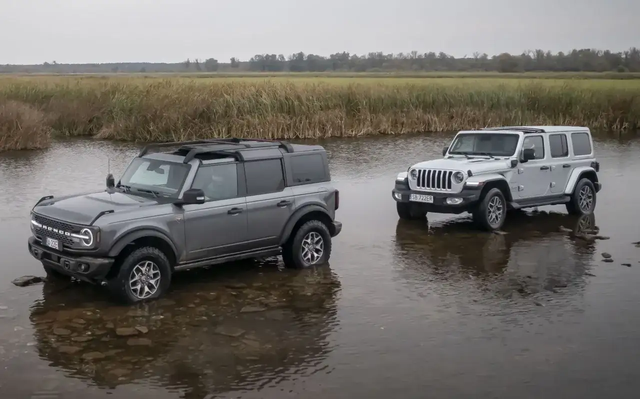 Szary Ford Bronco i biały Jeep SUV stoją w płytkiej wodzie, gotowe na przygodę.