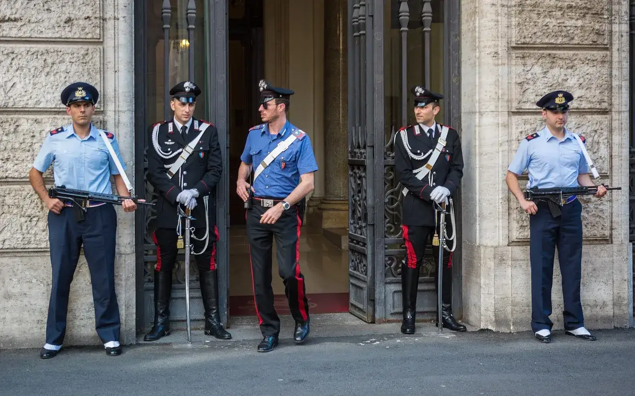 Carabinieri in divisa, alcuni con fucile, altri con sciabola, sorvegliano un ingresso. Il loro stipendio &egrave; meritato per la dedizione.