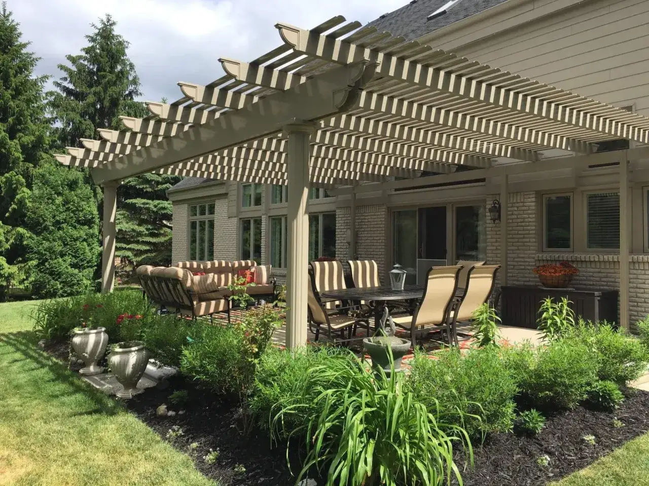 A beautiful patio with a pergola, perfect for awning installation, features outdoor seating and lush landscaping.