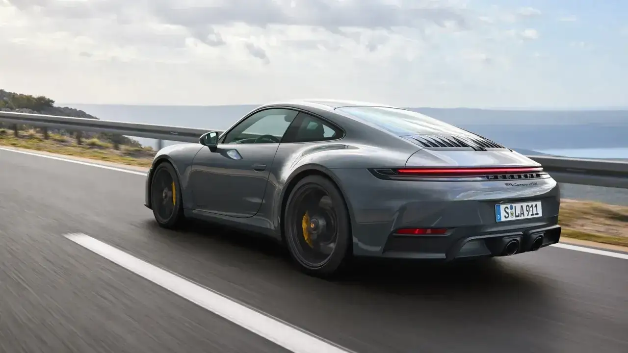 Szary Porsche 911 GTS pędzi po krętej drodze nad morzem.