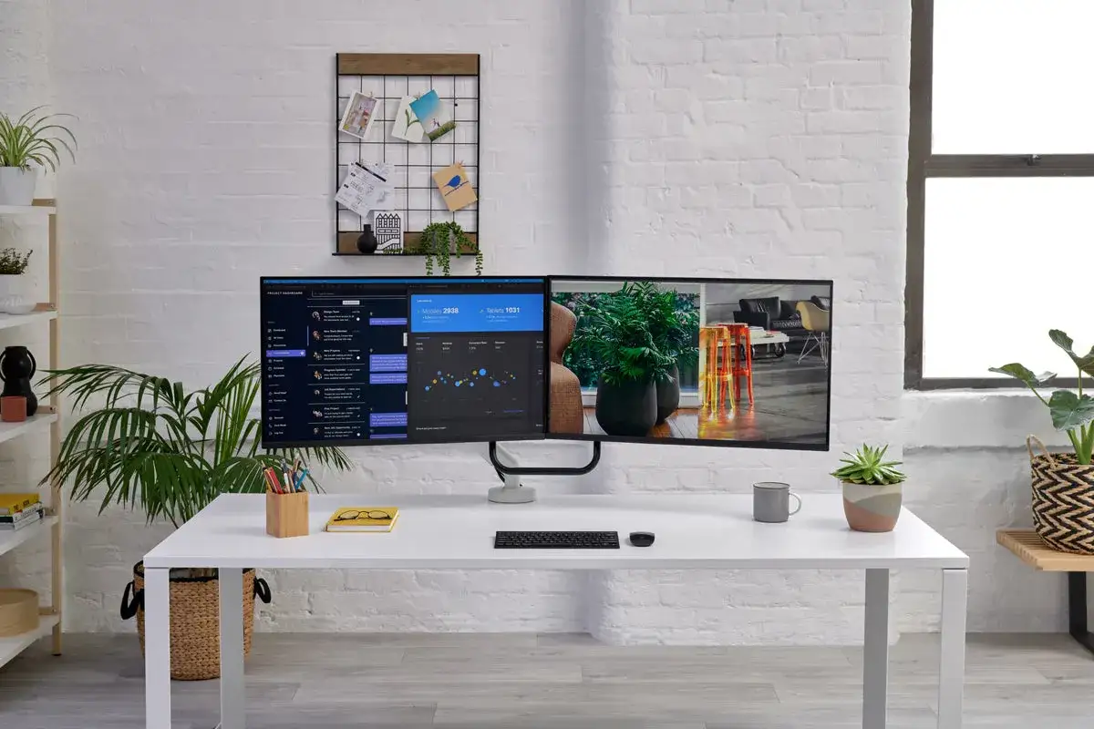 Bureau moderne avec un double écran PC affichant des données et une image d'intérieur. Des plantes vertes apportent de la vie à l'espace.