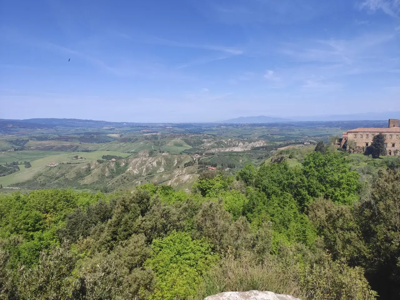 Panoramica mozzafiato delle balze di Volterra, con dolci colline verdi, un antico edificio e un cielo azzurro limpido.