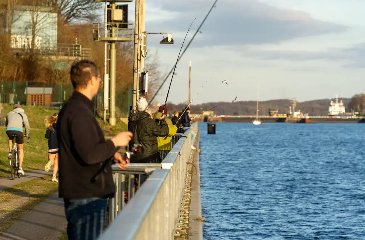Angler am Kai in Stralsund hoffen auf Hering. Im Hintergrund fahren Schiffe auf dem Wasser.