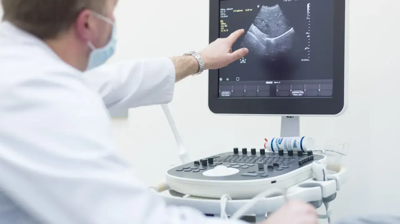 Lekarz w masce wskazuje palcem na obraz USG, przygotowując się do biopsji aspiracyjnej.