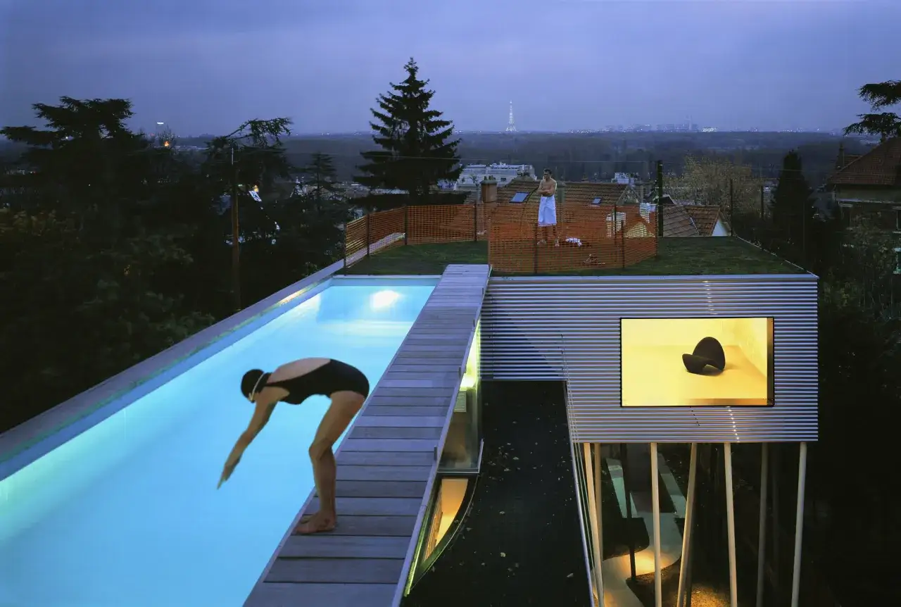 La Villa Dall'Ava, une femme se pr&eacute;pare &agrave; plonger dans la piscine illumin&eacute;e, avec Paris en toile de fond.