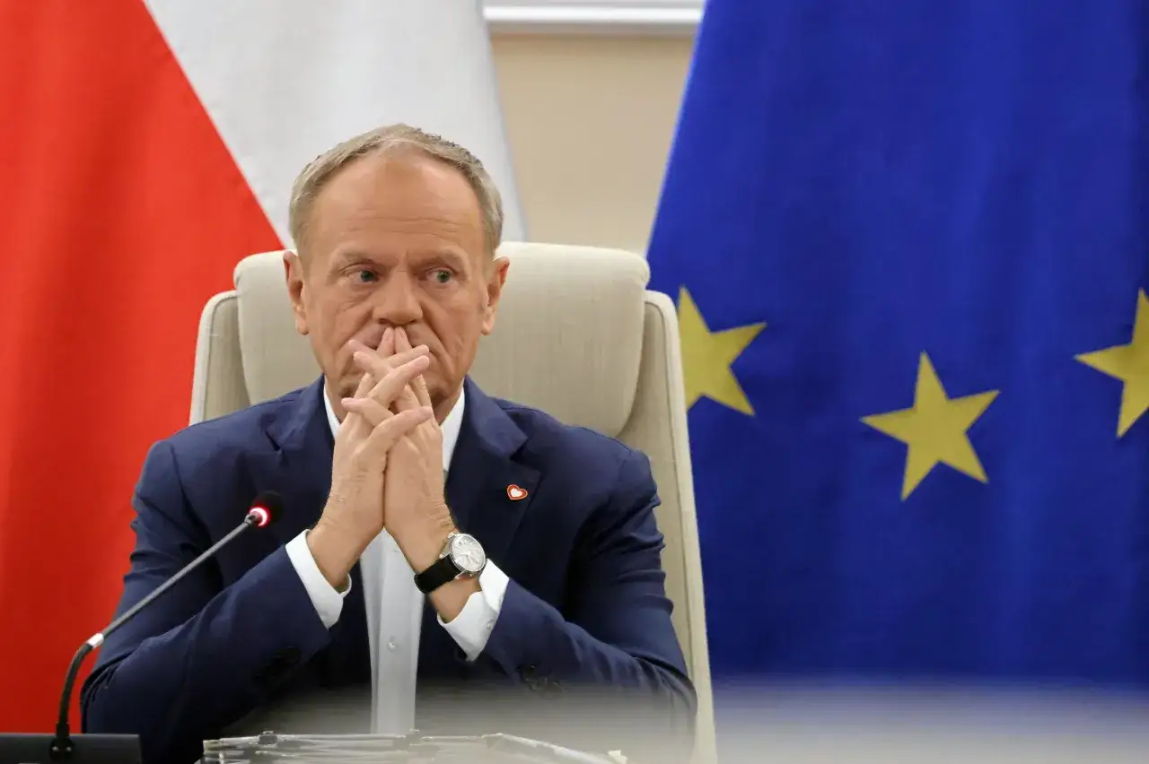 Premier Tusk z rękami złożonymi na ustach, w tle flagi Polski i UE. Zastanawia się, kiedy kończy się kadencja premiera Tuska.