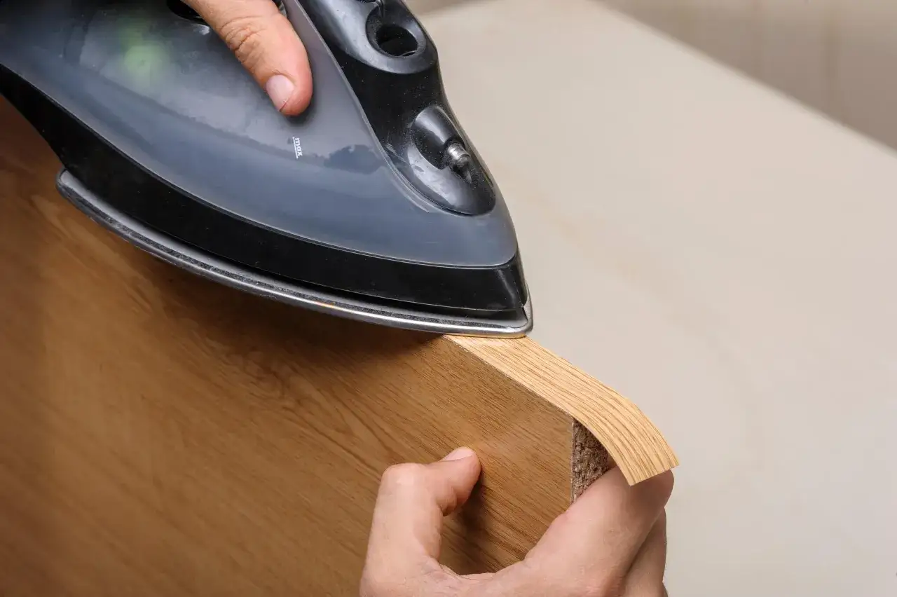 Persona aplica cinta de cantear a un tablero de madera con una plancha.