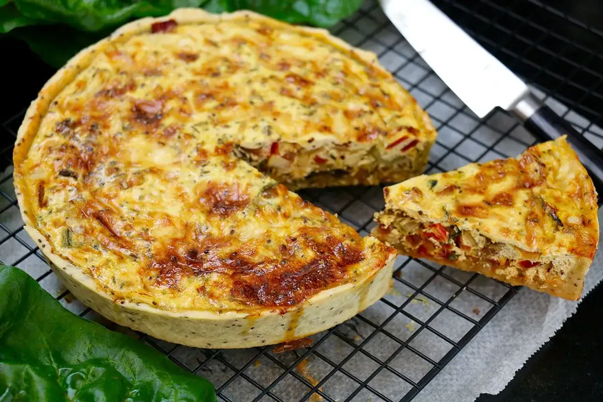 Une délicieuse quiche aux légumes dorée, avec une part coupée, prête à être dégustée.
