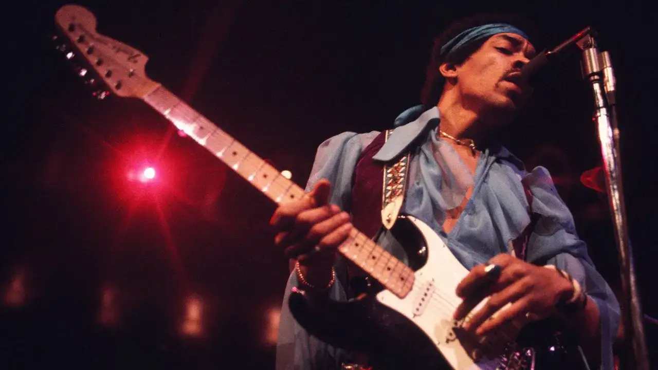 Jimi Hendrix, icône du rock, joue de sa guitare électrique dans un style de musique inimitable, baigné de lumières rouges.