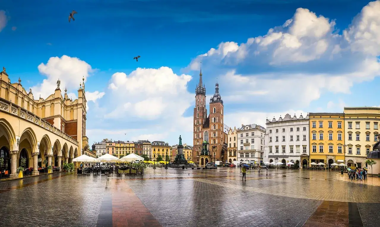 Rynek Główny w Krakowie z Sukiennicami, Kościołem Mariackim i kolorowymi kamienicami. Deszcz odbija się w bruku, tworząc magiczną atmosferę.