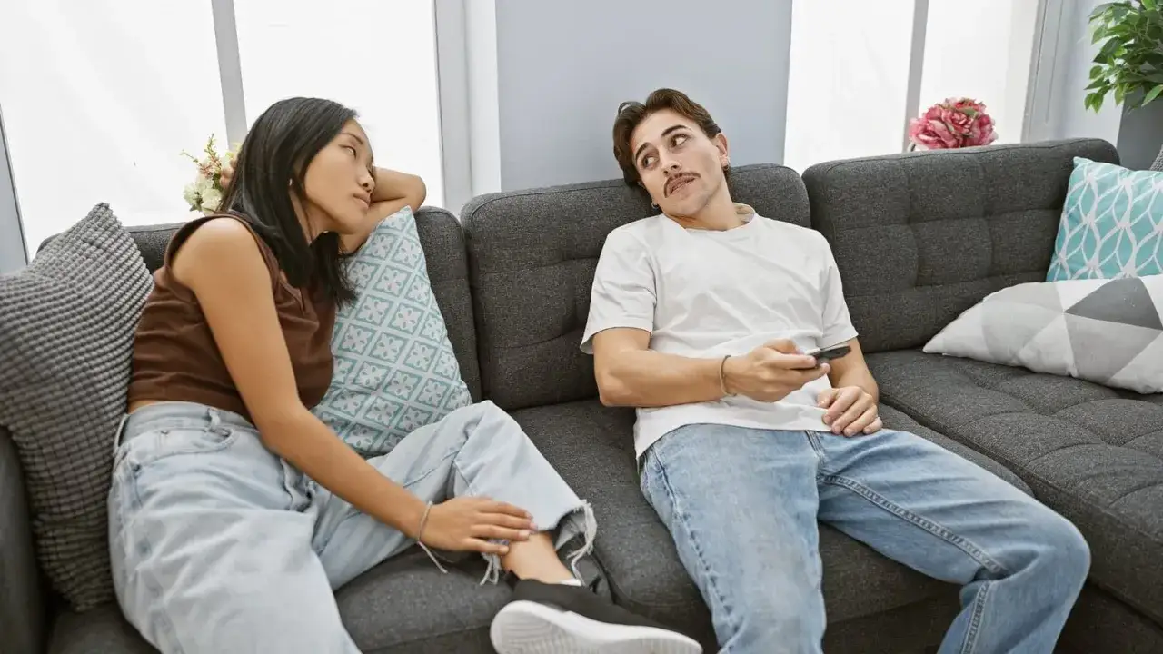 Un couple sur un canap&eacute;. Elle le regarde, pensant : 