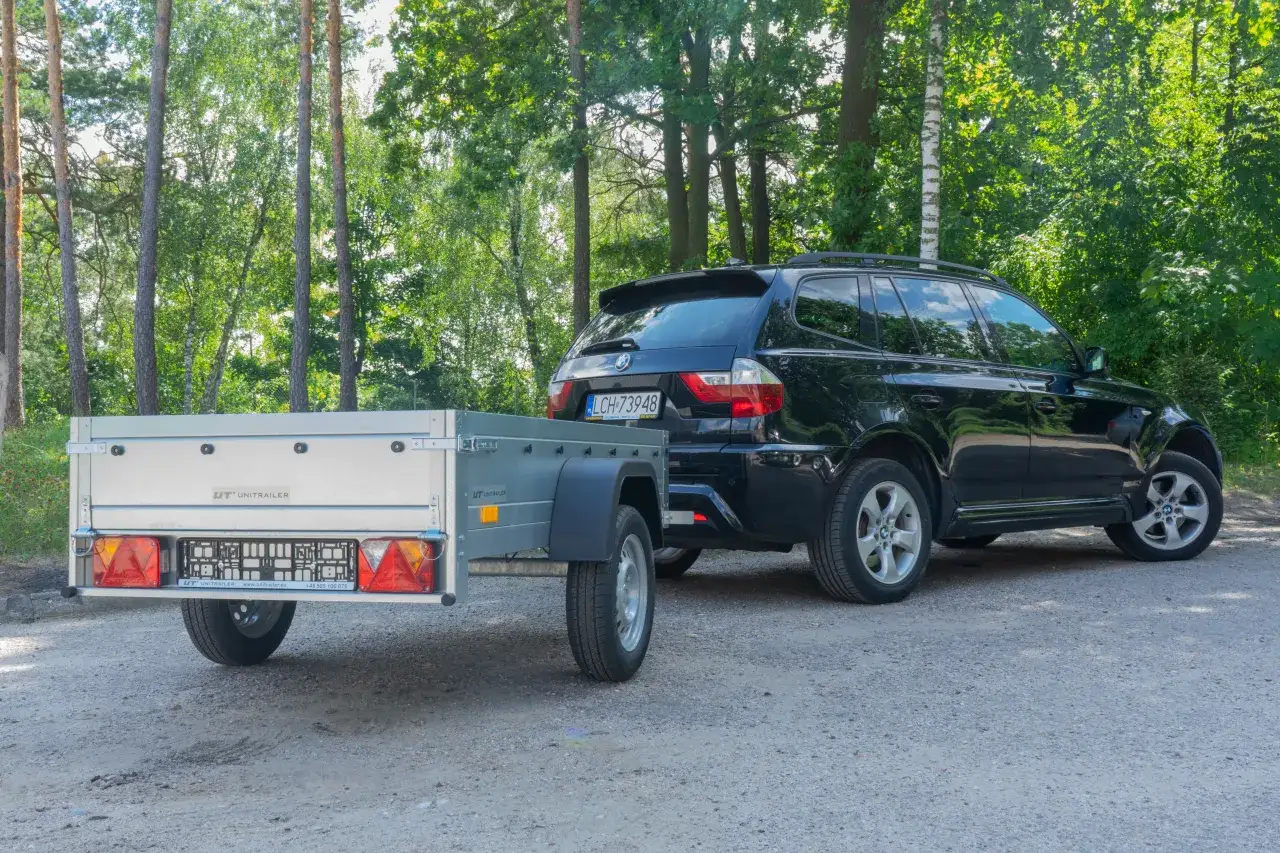 Czarny SUV z przyczepką kempingową na leśnej drodze. Zastanawiasz się, ile kosztuje przegląd przyczepki?