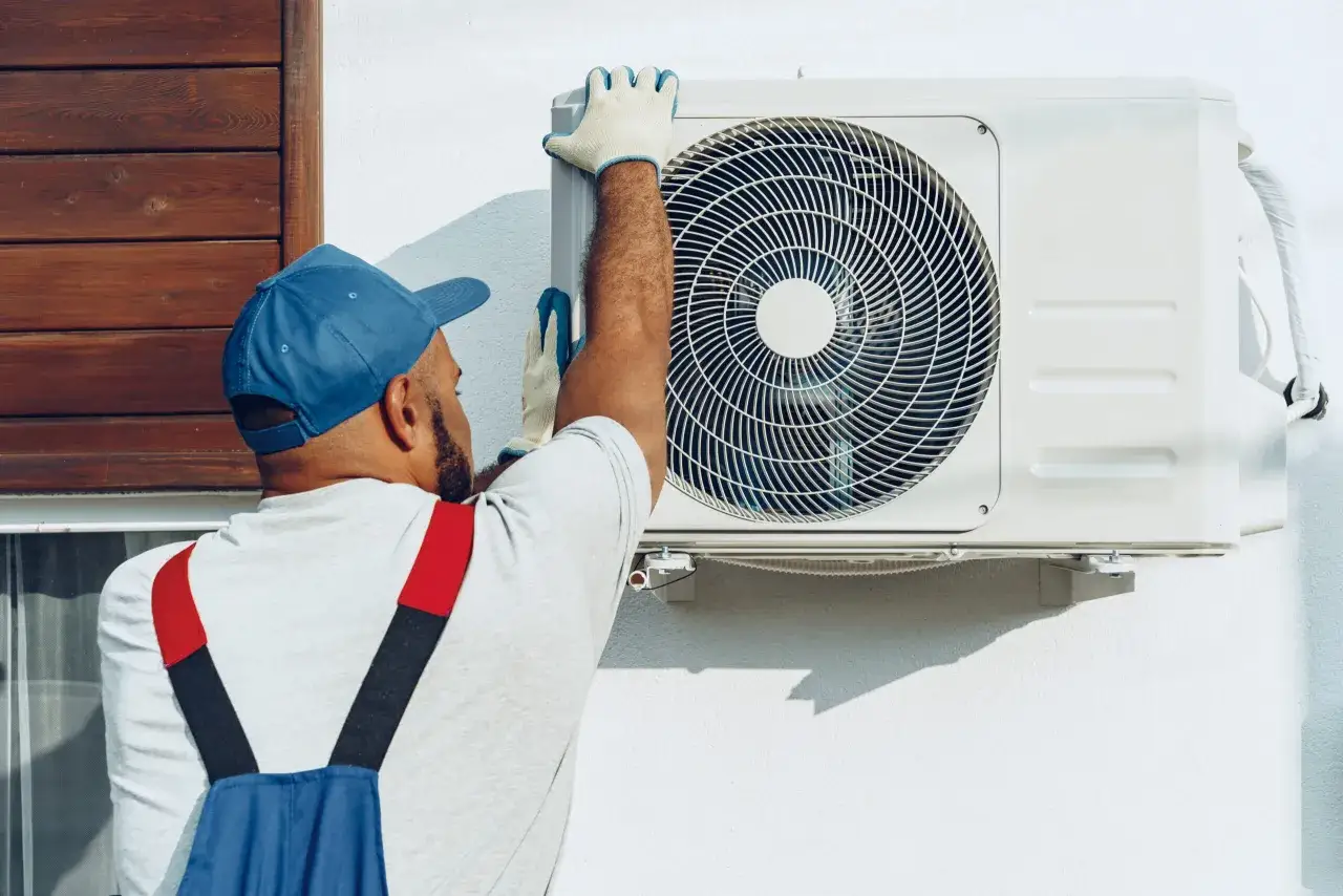 Technicien en bleu effectuant l'entretien d'une pompe à chaleur air eau. Il ajuste la façade de l'unité extérieure.