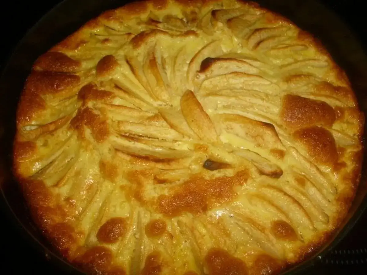 Ein goldbrauner Apfelkuchen mit Schmandguss, dessen Äpfel kunstvoll angeordnet sind.