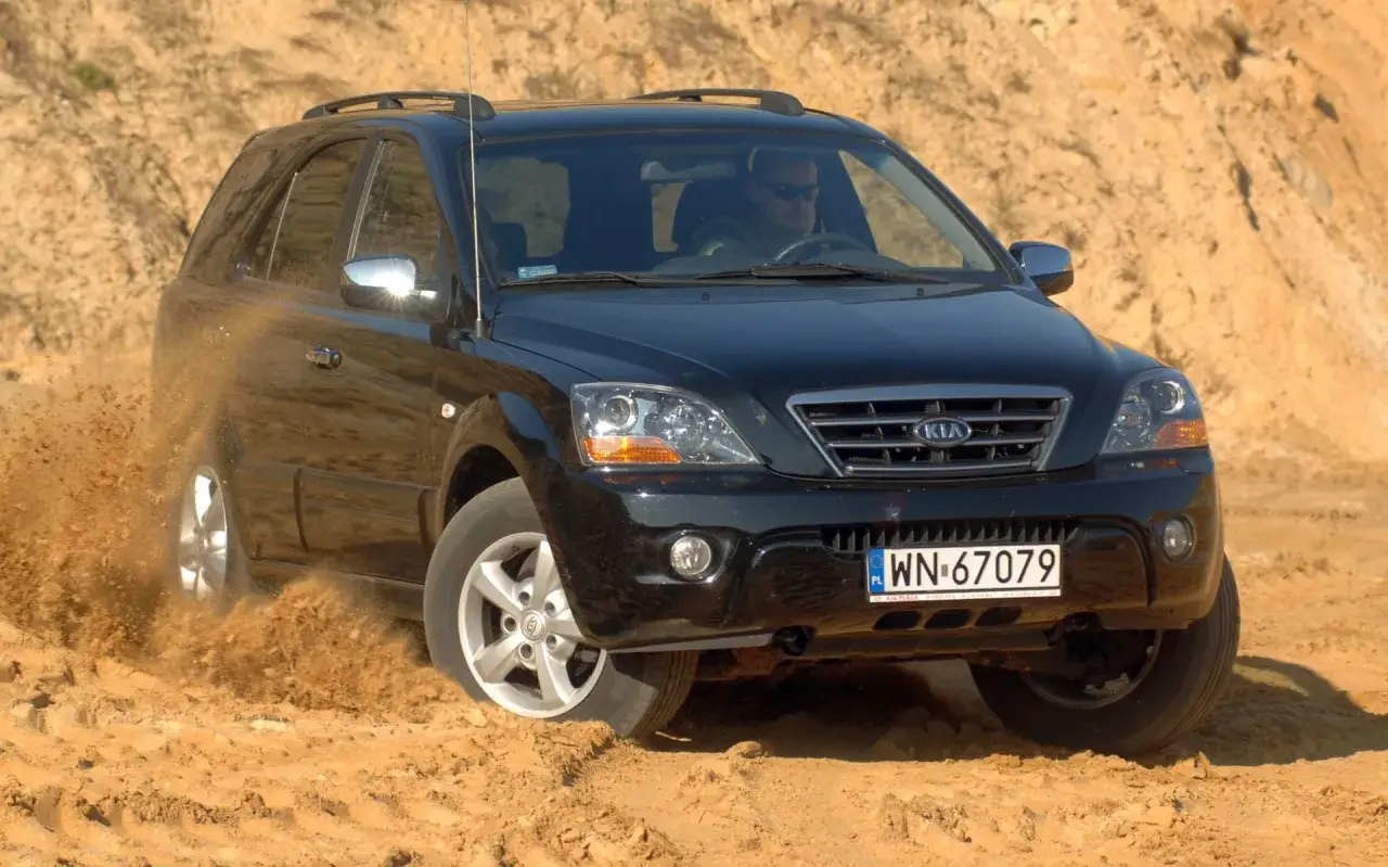 Czarny Kia Sorento 1. pokonuje piaszczysty teren, wzbijając tumany kurzu.