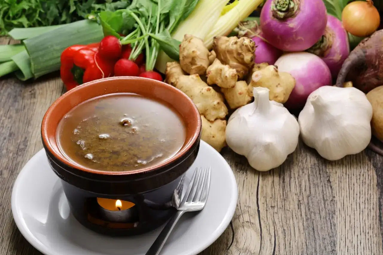 Una ciotola di bagna cauda calda, con verdure fresche come topinambur, aglio, rape e peperoni sullo sfondo.