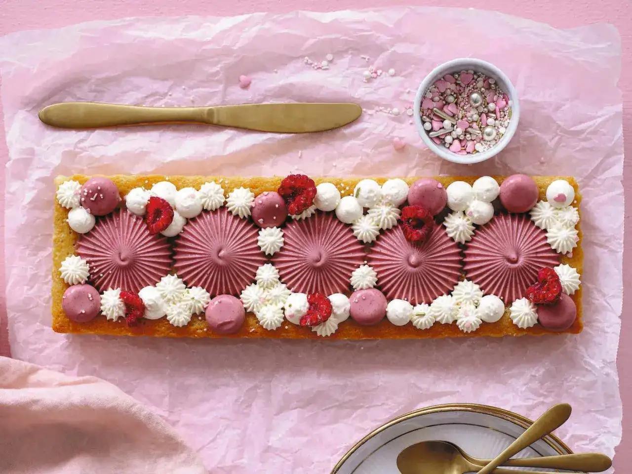 En avlång citron kladdkaka dekorerad med rosa frosting, hallon och vita gräddtoppar. En festlig tårta för alla tillfällen.