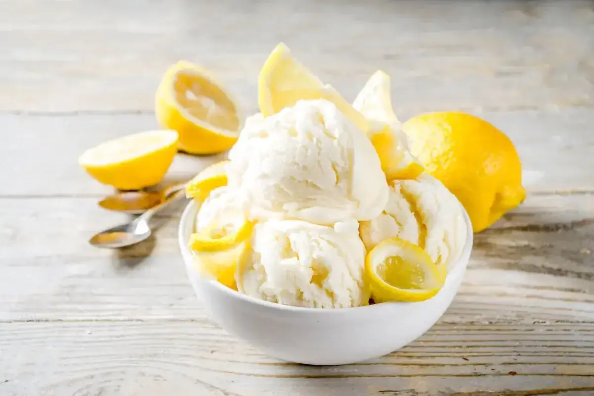 Coppa di gelato al limone bimby, guarnita con spicchi e scorzette di limone fresco, su un tavolo di legno chiaro.