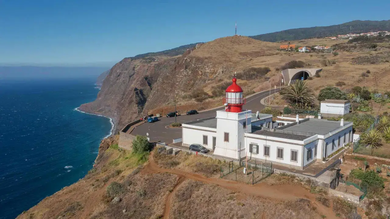 Leuchtturm am Ponta do Pargo, Madeira, ragt über steile Klippen. Das Meer glitzert blau, eine Straße schlängelt sich vorbei.
