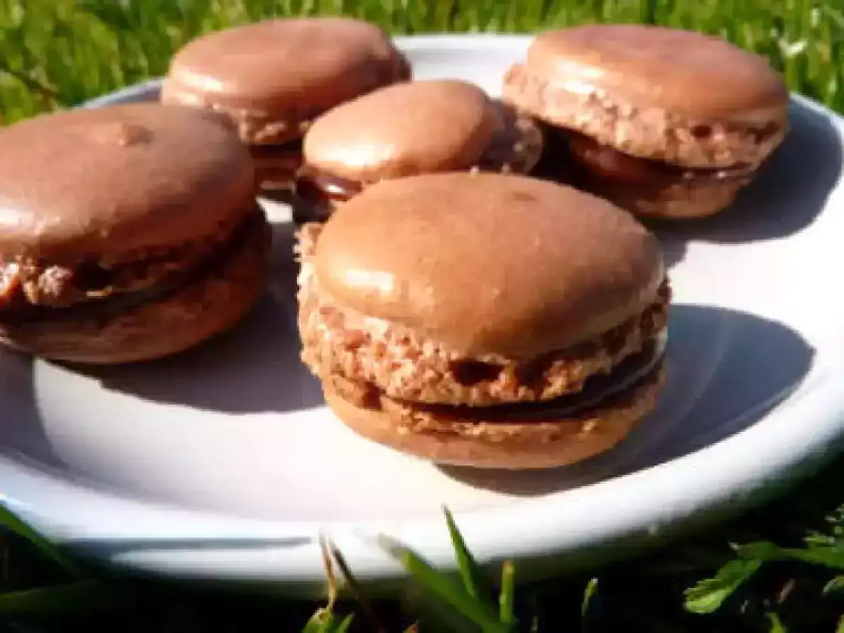 Cinq macarons au chocolat, avec une garniture crémeuse de ganache carambar, sur une assiette blanche.